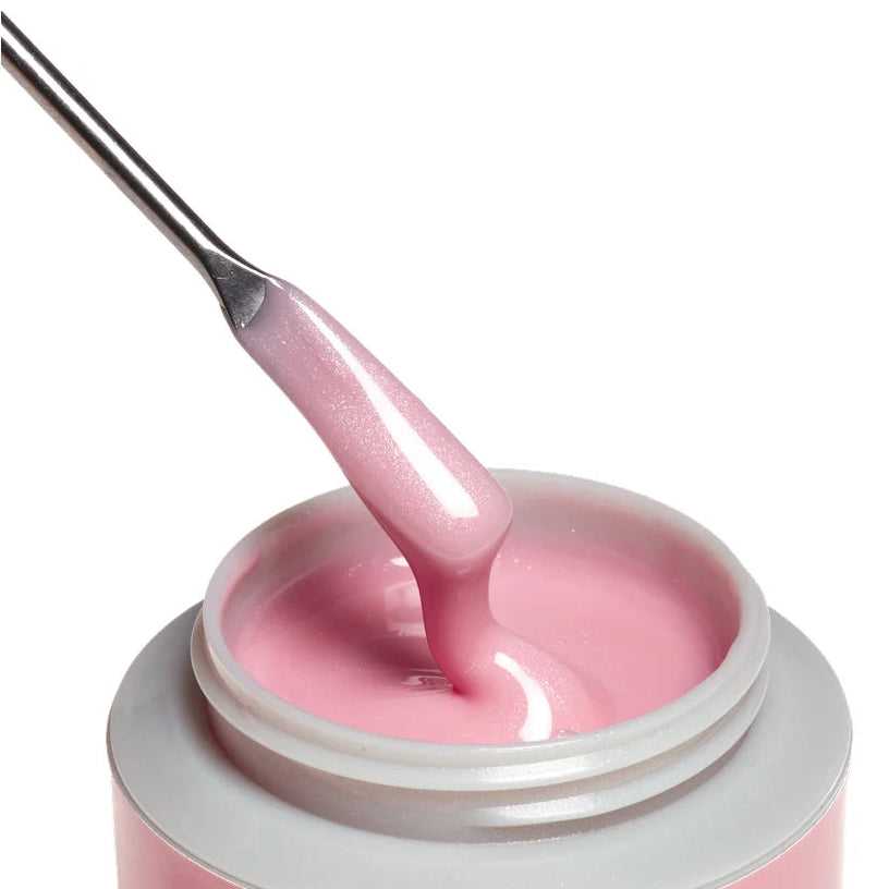 A close-up of a pink nail gel or acrylic product in an open jar, with a metal spatula lifting a glossy, slightly shimmering pink swatch of the material above the container, on a white background.