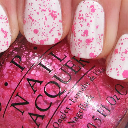 Close-up of a hand with white nails featuring pink speckles, holding a bottle of OPI nail polish.